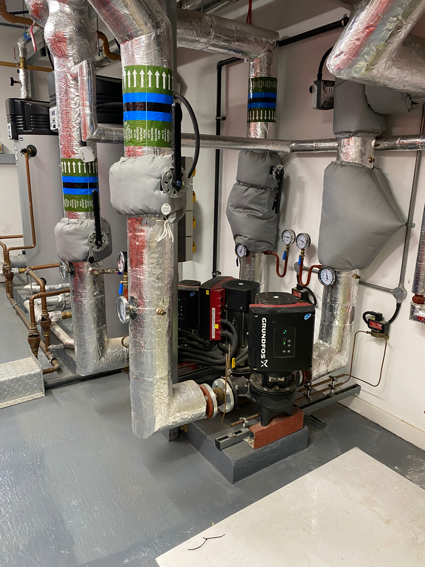 Grundfos commercial circulation pump installed in a London plant room with insulated LTHW flow and return pipework, pressure gauges and isolation valves