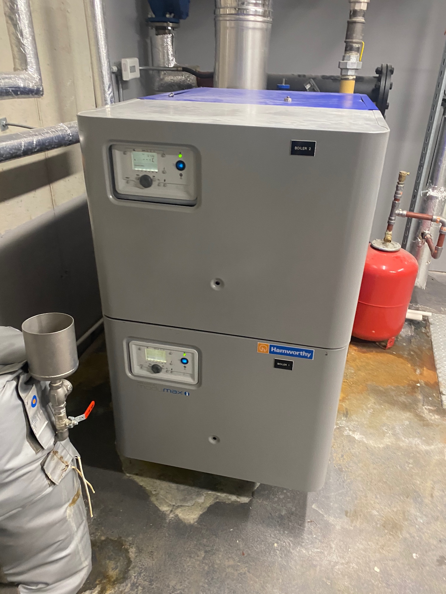 Stacked Hamworthy Modumax floor-standing commercial boilers installed in a London plant room with flue connections and gas isolation