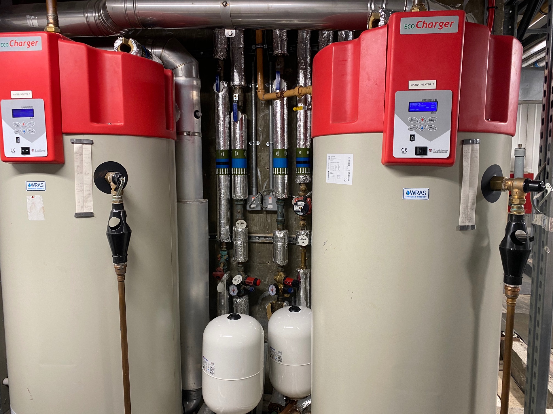 Twin Lochinvar EcoCharger gas-fired commercial water heaters installed in a London plant room with insulated flow, return and DHW pipework, expansion vessels and WRAS-approved fittings